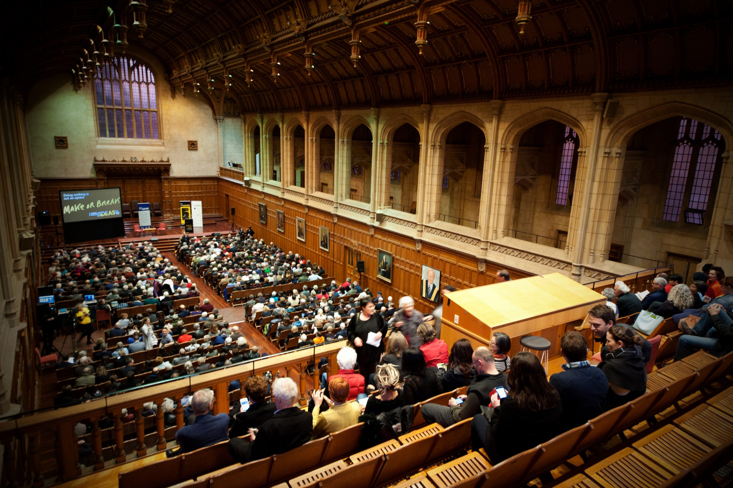 A large crowd sits patiently in an ornate hall